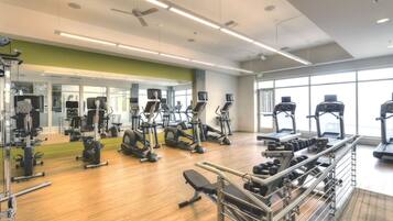 A gym with various exercise equipment, a mirrored wall, and large windows.