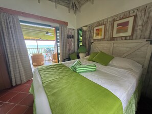A bedroom with a bed, green pillows, a green and white striped blanket, a wooden headboard, and a view of the sea through a window. - Stunning, Beachfront, Sunset Views, Turtle Point 4 bedroom villa W Private Pool (Port Elizabeth)