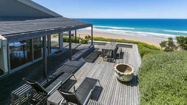 A wooden deck with outdoor furniture overlooking a beach and ocean. - The Cliff's Edge (Fairhaven)