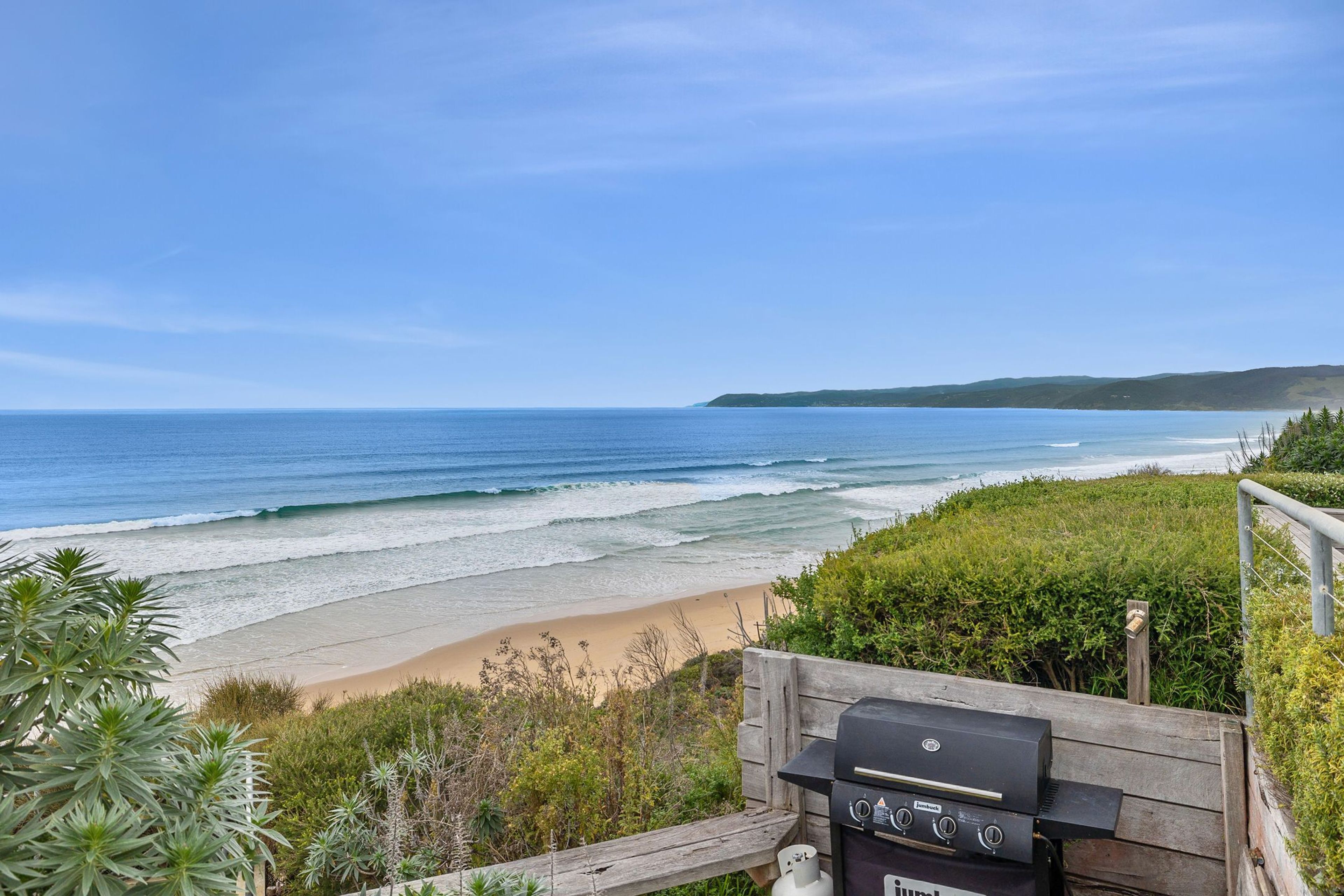 A beach view with a barbecue grill on a wooden deck.