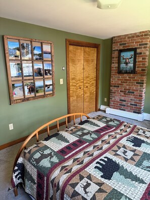 Ein Zimmer mit einem hölzernen Bett, einer gesteppten Decke, einem Kamin aus Ziegelsteinen und einer gerahmten Fotocollage an der Wand.