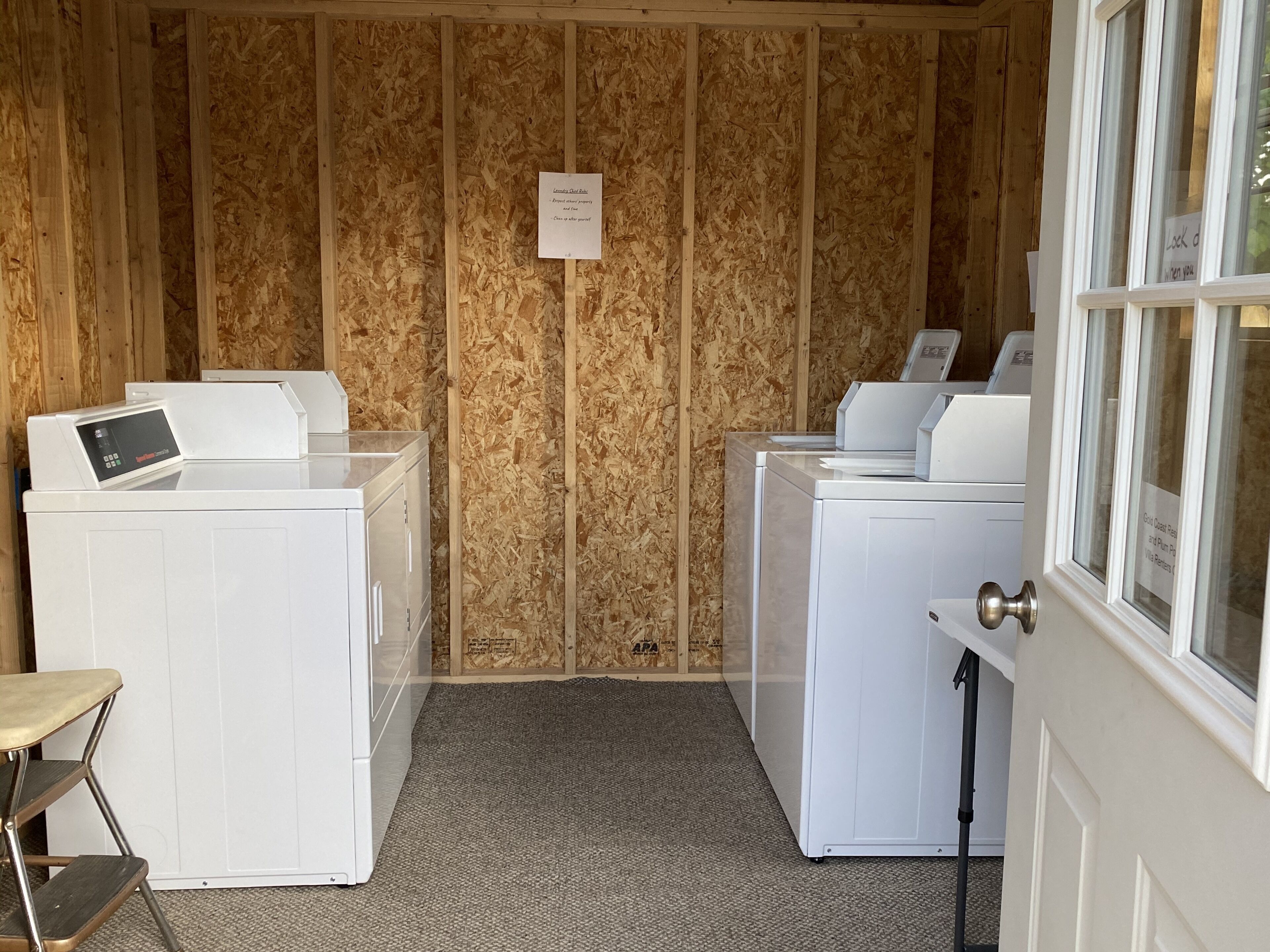 A laundry room with two white washing machines, a step stool, and a door with a window.