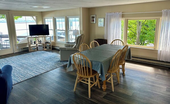 A dining area with a table and chairs, a television, and large windows with curtains.