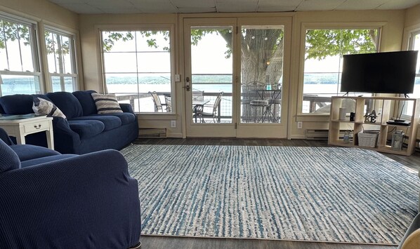 A living room with a blue sofa, a TV, and a view of the outdoors through large windows.