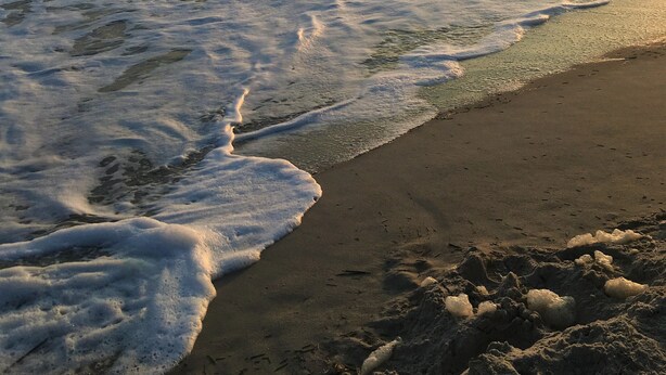 Platja amb onades que s'aproximen a la riba, cel serè i un capvespre.