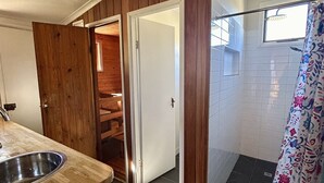 Ein Badezimmer mit Dusche, Waschbecken und einer Tür zu einem Holzraum.
