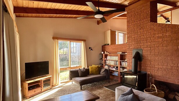 Ein gemütliches Wohnzimmer mit Kamin, Holzbalkendecke und großem Fenster.