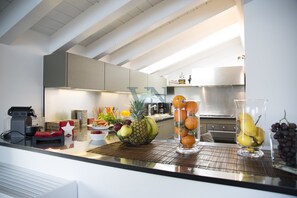 A modern kitchen with a fruit bowl, a coffee maker, and a glass of fruit on the counter.
