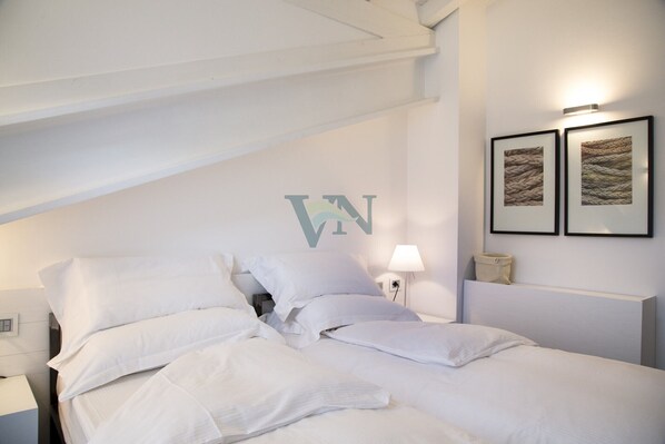 A neatly made bed with white linens, a wall-mounted light, and two framed pictures on the wall. - Spacious Penthouse With Front Terrace &, 5 Lake View Balconies (Menaggio)