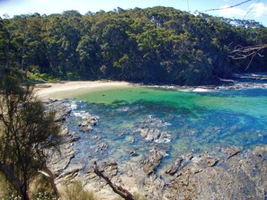 Un paysage côtier caractérisé par une eau turquoise cristalline, une plage de sable et une forêt verdoyante et luxuriante.