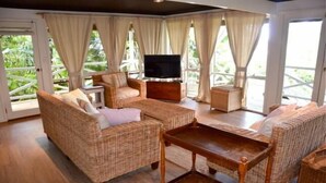 A cozy living room with wicker furniture, a flat-screen TV, and large windows with curtains. - Beautiful Beachfront Palm Beach Style House (Rosedale)