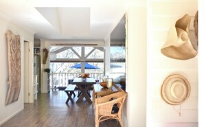 A room with a wooden floor, a dining table with chairs, a large window with a view of trees, and a wall-mounted hat. - BEACHFRONT OASIS.4 BEDROOMS. SLEEPS 14.PETS WELCOME. (Rosedale)