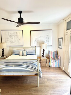 A bedroom with a bed, two wall-mounted lamps, a ceiling fan, and two framed architectural drawings.