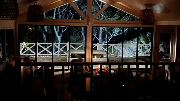 A cozy interior with a wooden ceiling, large windows, and a view of an outdoor deck. - Beautiful Beachfront Palm Beach Style House (Rosedale)