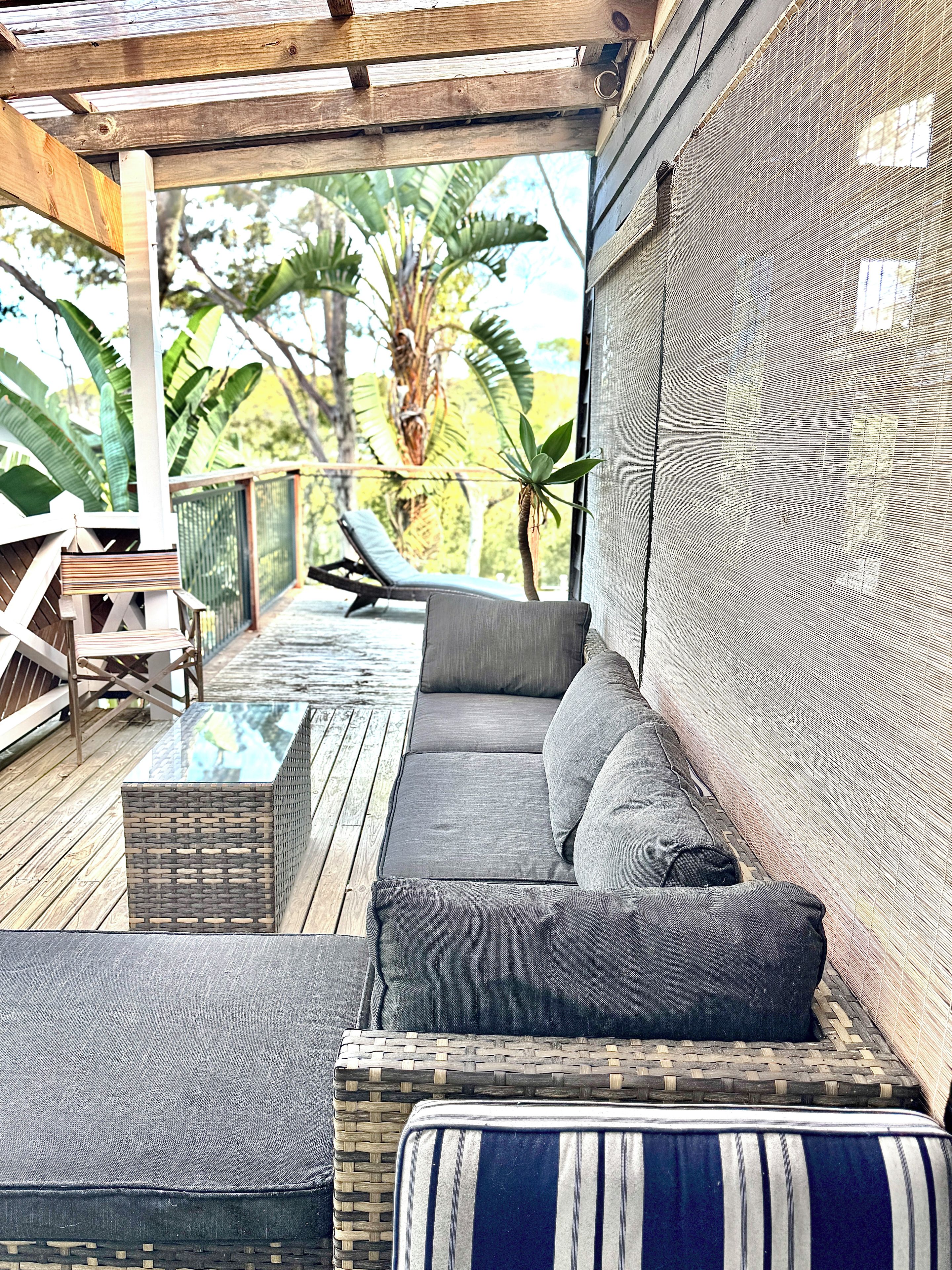 Un espace extérieur aménagé, abrité et doté d’un canapé et de fauteuils, d’une table à plateau en verre, et offrant une vue sur la végétation tropicale.