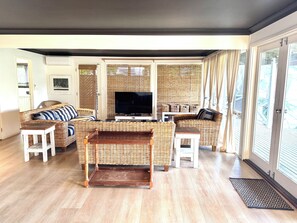 Un salon avec des meubles en osier, un téléviseur à écran plat et une porte-fenêtre coulissante donnant sur un balcon.