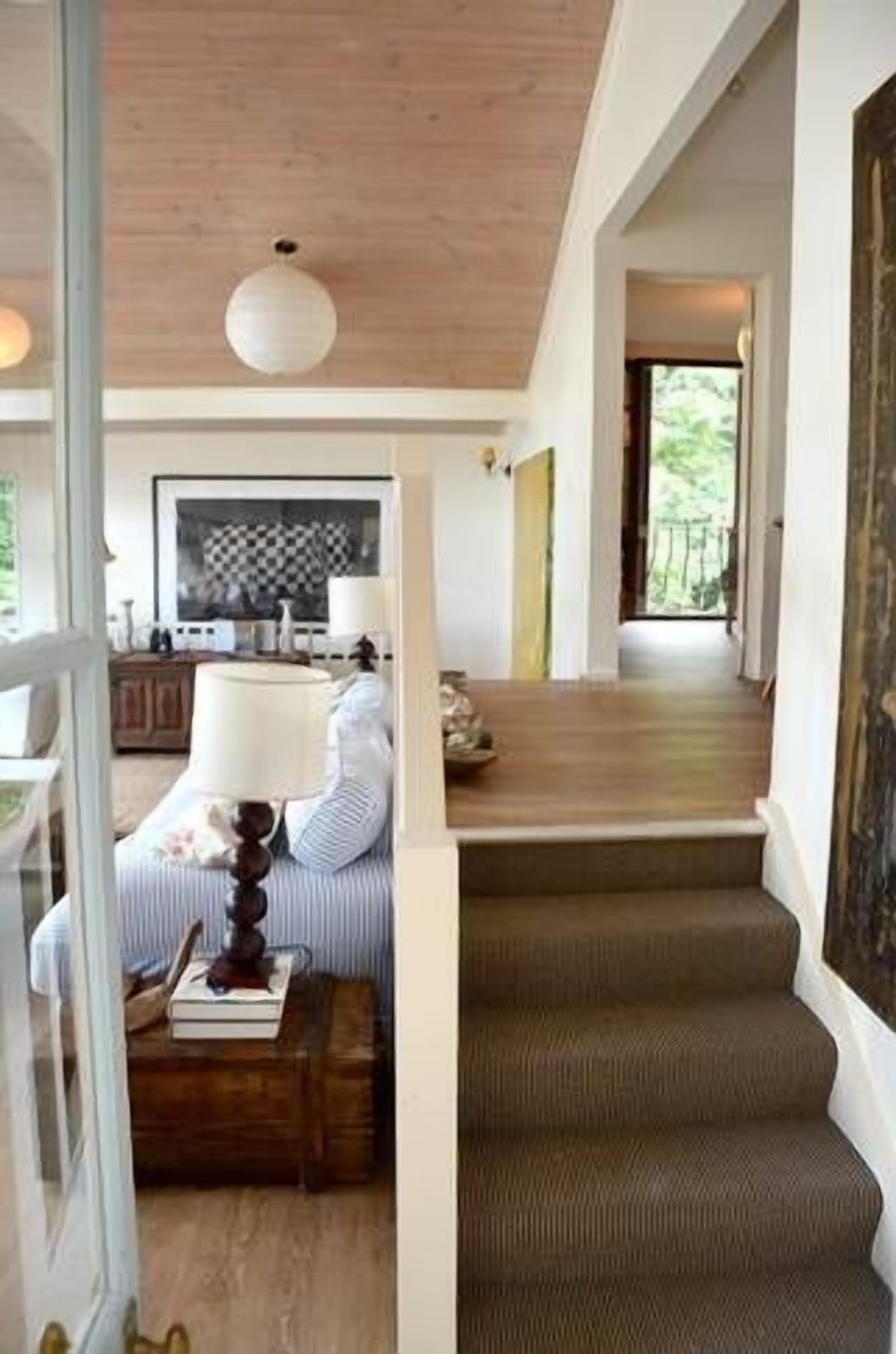 Un escalier menant à un deuxième étage, dont les marches sont recouvertes de bois, un coin repas avec une nappe à carreaux et une lampe posée sur une table d’appoint.