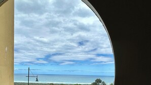 A view through a circular window of a road leading to a grassy area with a lamppost and a metal roof structure. - Large spacious house with many ocean views. Set in a peaceful quiet location. (Lake Bunga)