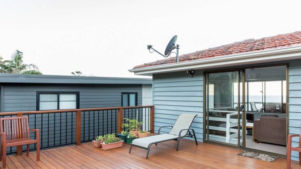Un balcón moderno con terraza de madera, una silla de descanso, una mesita con plantas en macetas y una antena parabólica.