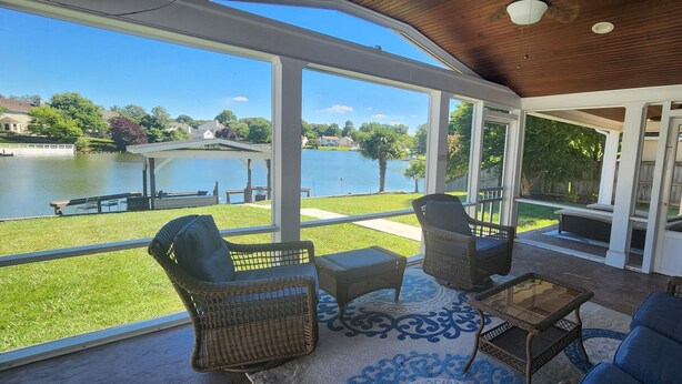 A covered patio with wicker furniture, a glass coffee table, and a view of a lake and houses. - Lakefront Oasis Centrally Located. Elegant, spacious and you're going to love it (Virginia Beach)