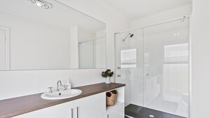 A modern bathroom with a white vanity, a glass shower enclosure, and a large mirror. - Sea View at Silver Sands - Sitting Pretty with Sea, Hills and Washpool Views (Aldinga Beach)
