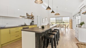 A modern kitchen with a central island, bar stools, and pendant lighting. - Sea View at Silver Sands - Sitting Pretty with Sea, Hills and Washpool Views (Aldinga Beach)