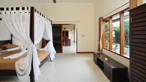 Een slaapkamer met een bed, een plafondventilator, een raam met uitzicht op groen en een houten bankje.