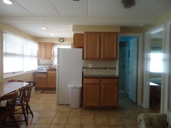 A kitchen with wooden cabinets, a white refrigerator, a microwave, and a dining area with chairs.