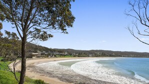 A coastal beach with a curved shoreline, a tree-lined path, and a backdrop of hills and residential buildings. - Cumberland Resort Lorne private Apartment near beach, pool, spa, tennis, shops (Lorne)