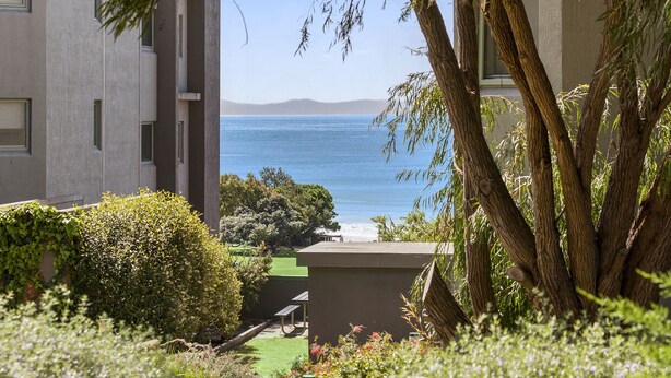 A view from a balcony overlooking a body of water with a distant mountain range, surrounded by greenery and a building facade. - Cumberland Resort Lorne private Apartment near beach, pool, spa, tennis, shops (Lorne)