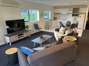 A modern living room with a flat-screen TV, sofas, a coffee table, and a kitchen in the background.
