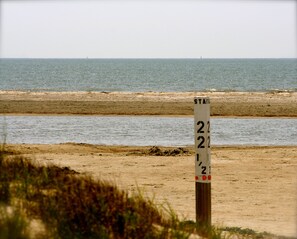 Uma praia com um poste de sinalização indicando um local, uma faixa de areia e o oceano ao fundo.