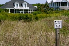 Placa indicando 'SULIVAN'S ISLAND STATION 22.5 ACCESS', com uma casa e grama alta ao fundo.