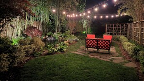 Un jardín con un estanque, bambú e iluminación con luces colgantes.