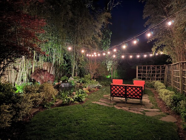 A garden with a pond, bamboo, and string lights.