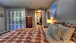 A bedroom with a plaid bedspread, a wooden wardrobe, a mirror, and a painting on the wall. - Sweet Suite! Modern, Pool, 2RM, 2BA, Ski Resort 532 (Killington)