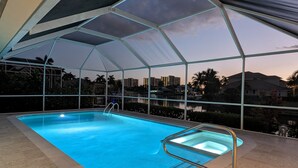 An indoor swimming pool with a glass ceiling, surrounded by a poolside area with a view of a cityscape and palm trees. - Avail August 28 & on. Sunny New heated Pool & Spa 10min walk2beach 6-bikes (Marco Island)
