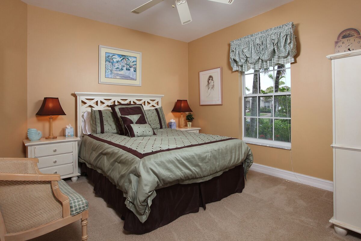 Une chambre à coucher comprenant un lit, deux tables de chevet, une chaise, une fenêtre avec vue et un ventilateur de plafond.
