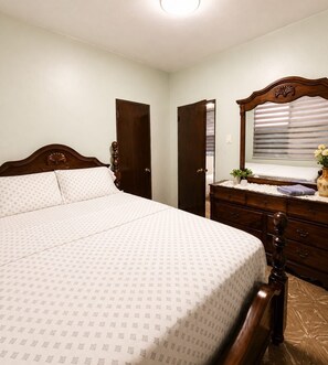 A bedroom with a bed, dresser, and a window with blinds.