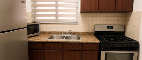 A compact kitchen with a refrigerator, microwave, double sink, stove, and oven.
