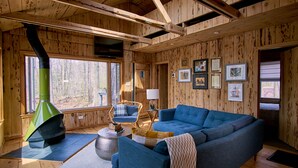 Ein gemütliches Blockhaus-Interieur mit einem blauen Sofa, einem Korbstuhl, einem Kamin und gerahmten Bildern an den Wänden.