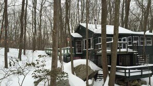 Eine Hütte mit vielen Fenstern und einem mit Schnee bedeckten Dach, umgeben von Bäumen und Felsen.