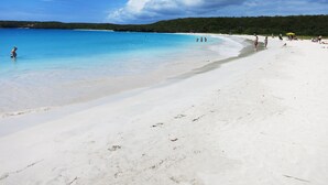 Une plage avec une eau d’un bleu limpide, du sable blanc et quelques personnes.