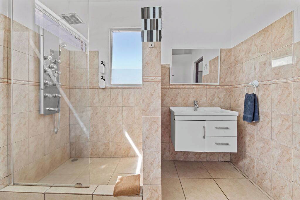A modern bathroom with a glass-enclosed shower, a white vanity with drawers, and a mirror above the sink.