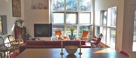 A modern living room with a large window, a sofa, a dining table, and red chairs.