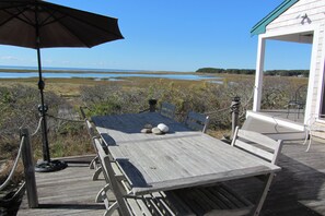 Enjoy outdoor dining or relaxation on the deck with a table and chairs, overlooking a serene body of water and distant shoreline.