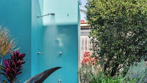 A turquoise door with a showerhead, surrounded by lush greenery and plants.