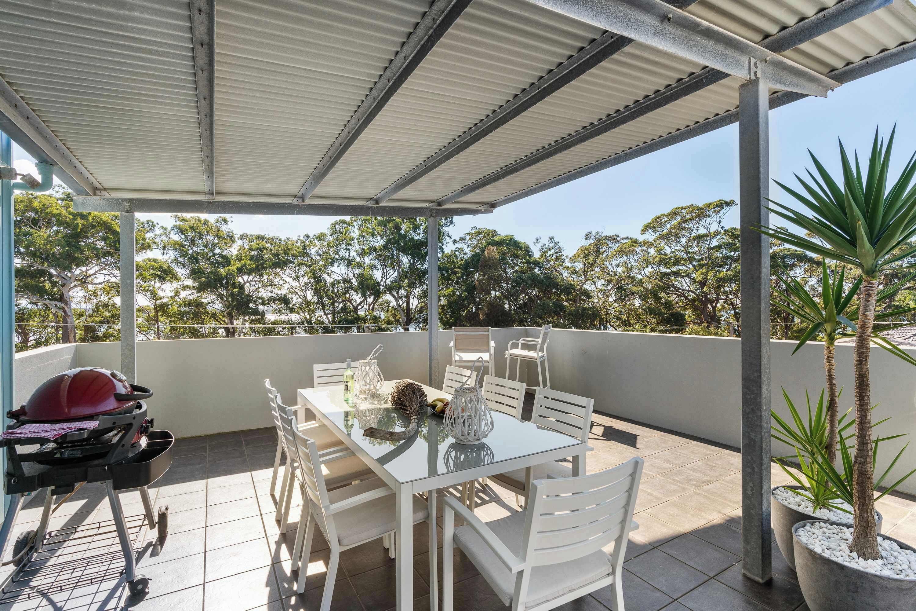 A covered outdoor patio with a table and chairs, a barbecue grill, and potted plants.