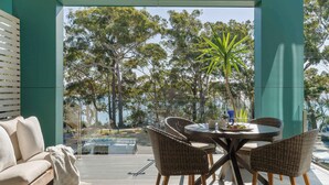 A covered outdoor seating area with wicker chairs and a table, overlooking a pool and trees.