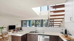 A modern kitchen with a dishwasher, a dining area with a glass table, and a staircase.
